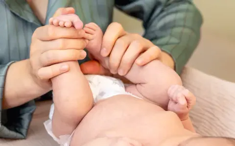 Mani che massaggiano le gambine di un neonato, un gesto d'amore per capire se il neonato ha le coliche e alleviare il suo disagio.