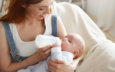 Mamma con capelli rossi allatta il suo bambino con un biberon. Impara come lavare i biberon per garantire l'igiene.