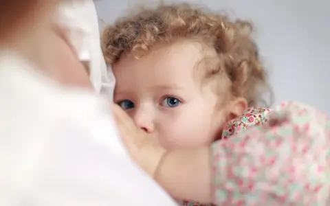 Bambina con occhi azzurri e capelli ricci, stretta al petto della madre. Un'immagine che evoca il legame profondo, ma anche le possibili conseguenze psicologiche dell'allattamento prolungato.