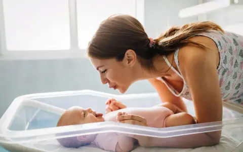 Mamma sorride al suo neonato nella culla. Un momento dolce che fa pensare a cosa mangiare dopo il parto per recuperare le energie.
