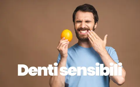 Uomo con espressione sofferente, tiene un'arancia e si tocca la guancia, mostrando i suoi denti sensibili al freddo.
