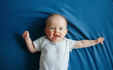 Un bimbo sorridente, con occhi azzurri e braccia aperte, celebra il suo scatto di crescita di 4 mesi su un telo blu.