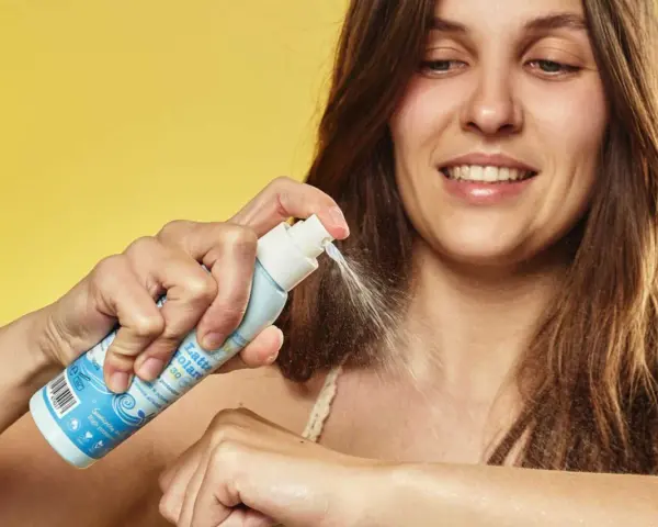 Donna sorridente applica latte solare spray SPF 50. La scelta di quale crema solare scegliere è facile con questo prodotto.