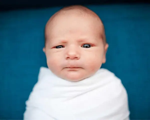 Primo piano di un neonato avvolto in una coperta bianca. La sua testa è quasi calva, mostrando una leggera perdita capelli neonato, tipica dei primi mesi.