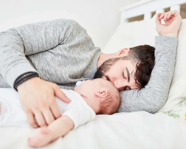 Padre e neonato nel lettone in sicurezza, un momento di dolce riposo e amore.