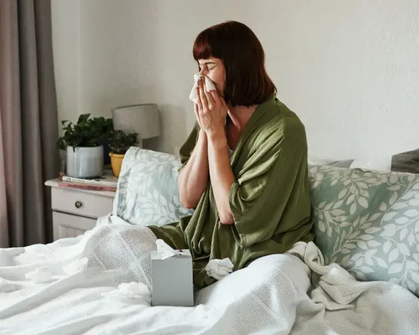 Donna a letto con fazzoletto, soffre di un raffreddore che non passa. Fazzoletti usati sparsi sul letto.