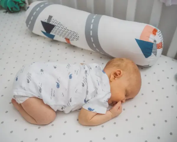 Dolce neonato dorme a pancia in giù, avvolto in un pigiamino con balene. Un cuscino decorato con navi lo accompagna nel sonno.