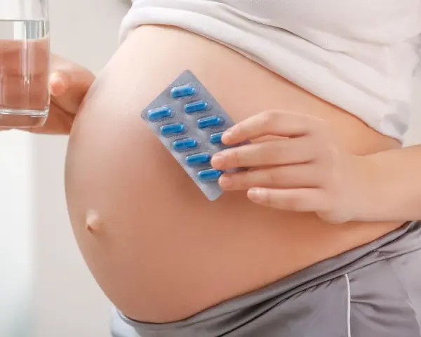 Pancia di donna incinta con blister di pillole blu e bicchiere d'acqua. Essenziale acido folico prima della gravidanza per la salute.