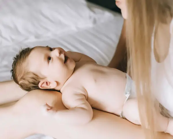 Un bimbo sorride sdraiato sulle gambe della mamma. Forse è l'inizio della lallazione, con le prime vocali che risuonano nell'aria.