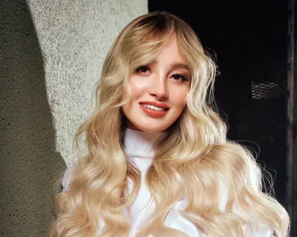 Ragazza con lunghi capelli biondi mossi, un sorriso radioso e labbra luminose. Nuovi colori per capelli che esaltano la sua bellezza naturale.