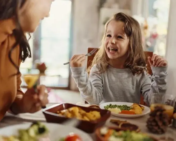 Bambina felice mangia da sola a tavola, mostrando che a che età i bambini mangiano da soli è un traguardo raggiunto con gioia.