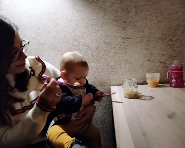 Mamma dà la pappa al suo bimbo fuori casa, con un vasetto di omogeneizzato e un biberon pronti.
