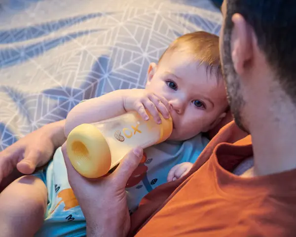 Un padre tiene un biberón per dare da mangiare al suo neonato. Il bambino afferra il biberon con le sue manine.