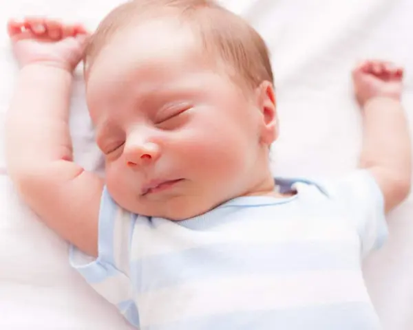 Un neonato dorme sereno con le braccia alzate. Sembra che i neonati possano mangiare mentre dormono, un vero miracolo della natura.