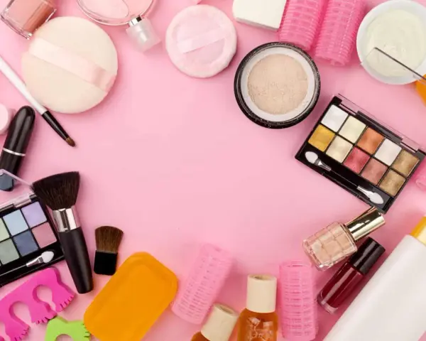 Tanti prodotti per il make-up, tra cui ombretti, rossetti e pennelli, disposti su sfondo rosa. Attenzione, gli ombretti scadono!