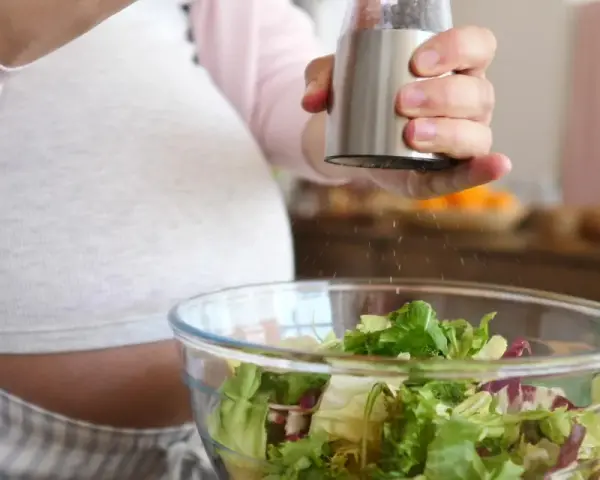 Donna incinta condisce un'insalata fresca. Ricorda come lavare frutta e verdura in gravidanza per una dieta sana.