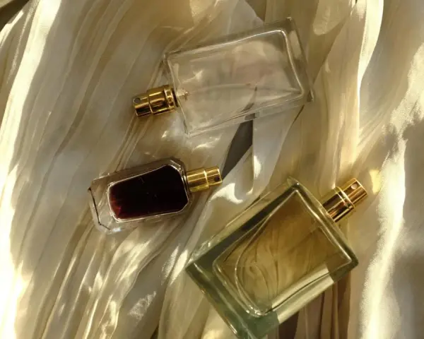 Flaconi di profumo su tessuto drappeggiato. Scopri come far durare di più il profumo con questi consigli.