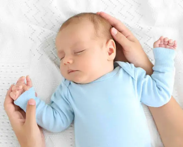 Un adorabile neonato dorme sereno sul fianco, cullato da mani amorevoli su una coperta bianca.