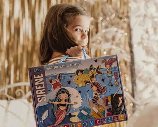 Bambina con scatola "Sirene Mega Box Arts & Crafts". A che età si impara a leggere? Forse con questo kit creativo, l'apprendimento sarà più divertente!