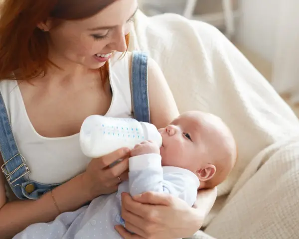Mamma con capelli rossi allatta il suo bambino con un biberon. Impara come lavare i biberon per garantire l'igiene.