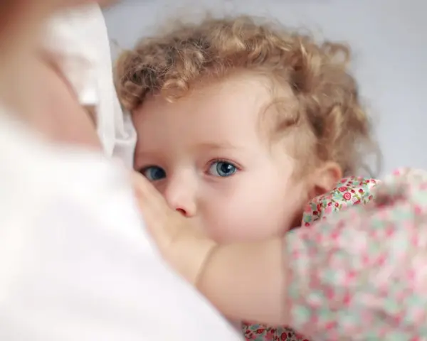 Bambina con occhi azzurri e capelli ricci, stretta al petto della madre. Un'immagine che evoca il legame profondo, ma anche le possibili conseguenze psicologiche dell'allattamento prolungato.