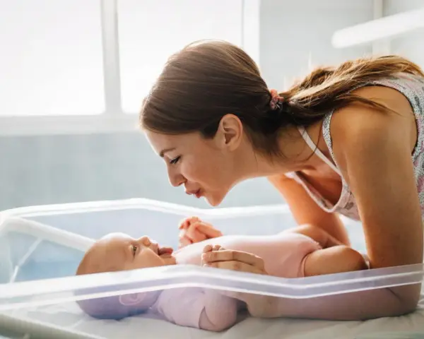 Mamma sorride al suo neonato nella culla. Un momento dolce che fa pensare a cosa mangiare dopo il parto per recuperare le energie.