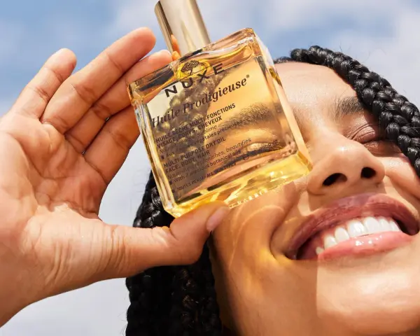 Una mano tiene una bottiglietta di Nuxe Huile Prodigieuse, un olio multiuso per viso, corpo e capelli. Scopri a cosa serve questo prezioso olio.