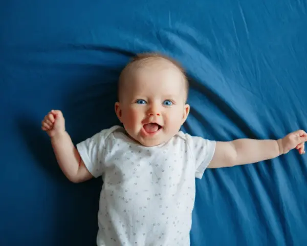 Un bimbo sorridente, con occhi azzurri e braccia aperte, celebra il suo scatto di crescita di 4 mesi su un telo blu.