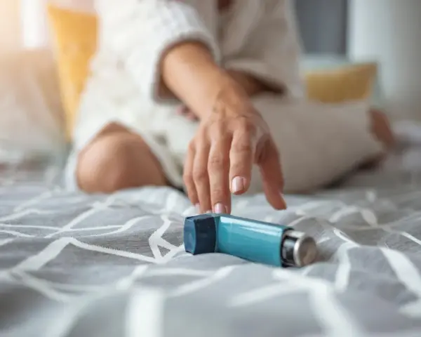 Mano tesa verso un inalatore blu, un aiuto per respirare. Il foster spray è pronto all'uso.