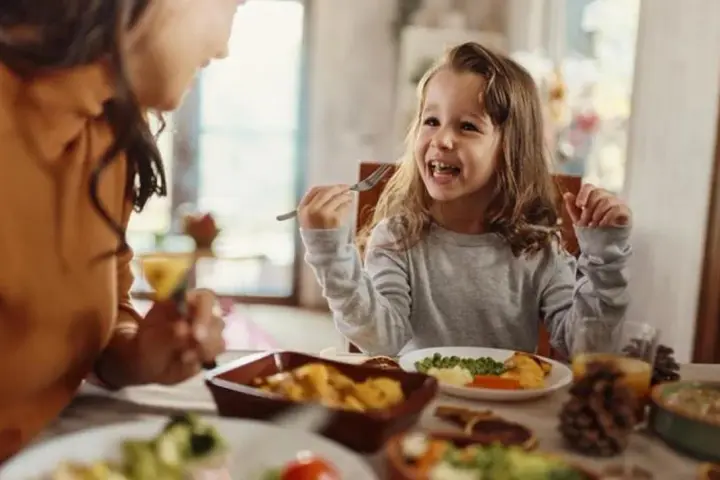 Bambina felice mangia da sola a tavola, mostrando che a che età i bambini mangiano da soli è un traguardo raggiunto con gioia.