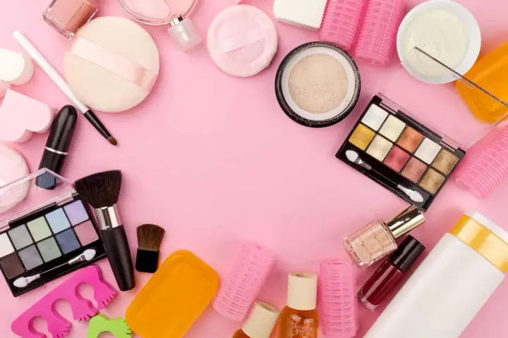 Tanti prodotti per il make-up, tra cui ombretti, rossetti e pennelli, disposti su sfondo rosa. Attenzione, gli ombretti scadono!
