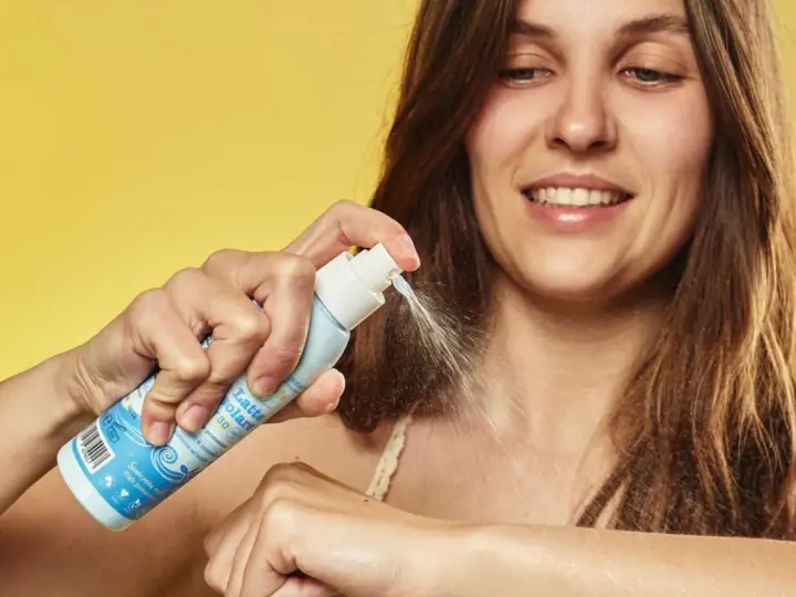 Donna sorridente applica latte solare spray SPF 50. La scelta di quale crema solare scegliere è facile con questo prodotto.