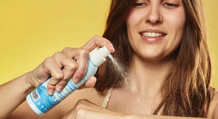 Donna sorridente applica latte solare spray SPF 50. La scelta di quale crema solare scegliere è facile con questo prodotto.