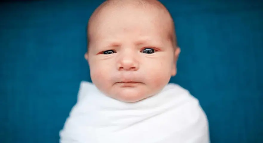 Primo piano di un neonato avvolto in una coperta bianca. La sua testa è quasi calva, mostrando una leggera perdita capelli neonato, tipica dei primi mesi.
