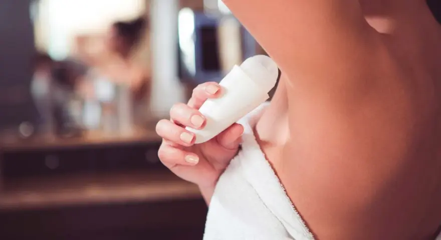 Mano femminile applica deodorante roll-on, con sali di alluminio per una protezione duratura.