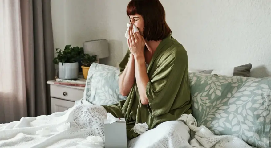 Donna a letto con fazzoletto, soffre di un raffreddore che non passa. Fazzoletti usati sparsi sul letto.
