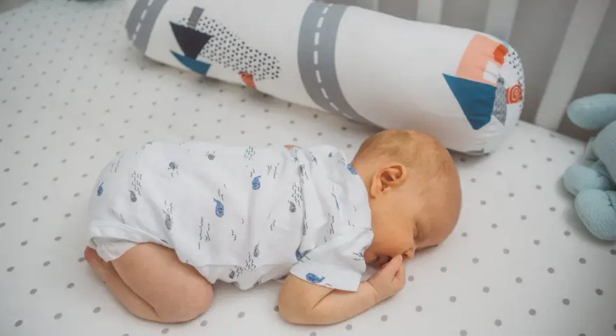 Dolce neonato dorme a pancia in giù, avvolto in un pigiamino con balene. Un cuscino decorato con navi lo accompagna nel sonno.