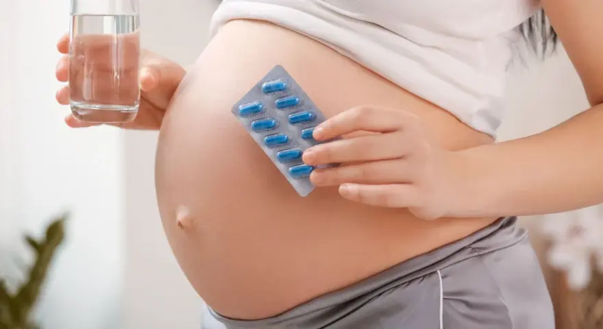 Pancia di donna incinta con blister di pillole blu e bicchiere d'acqua. Essenziale acido folico prima della gravidanza per la salute.