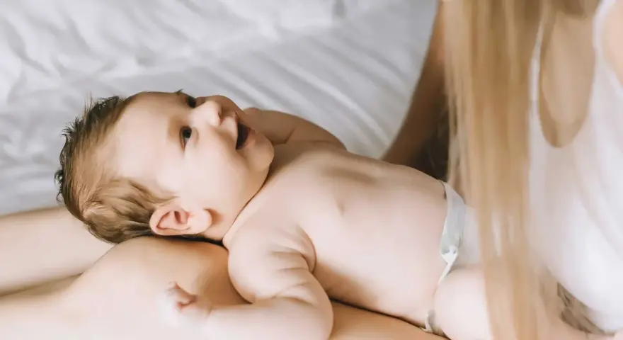 Un bimbo sorride sdraiato sulle gambe della mamma. Forse è l'inizio della lallazione, con le prime vocali che risuonano nell'aria.