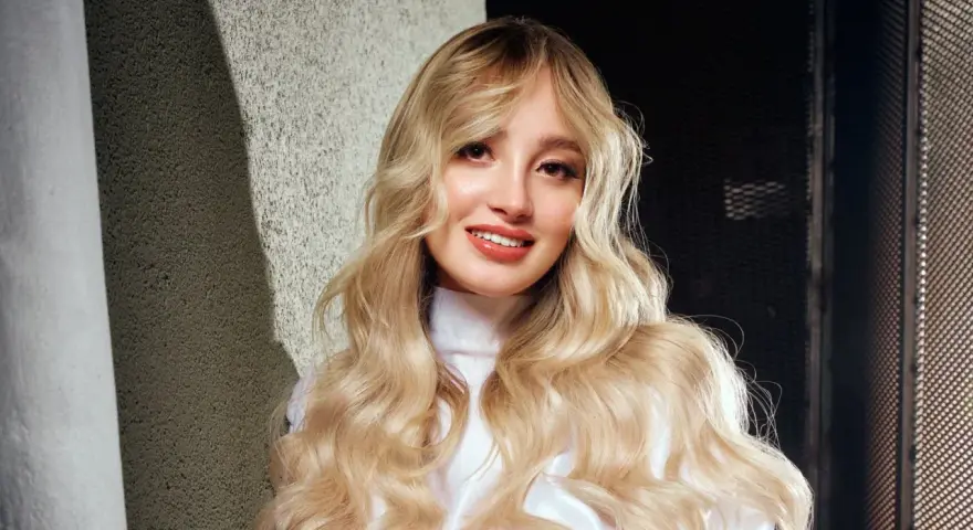 Ragazza con lunghi capelli biondi mossi, un sorriso radioso e labbra luminose. Nuovi colori per capelli che esaltano la sua bellezza naturale.