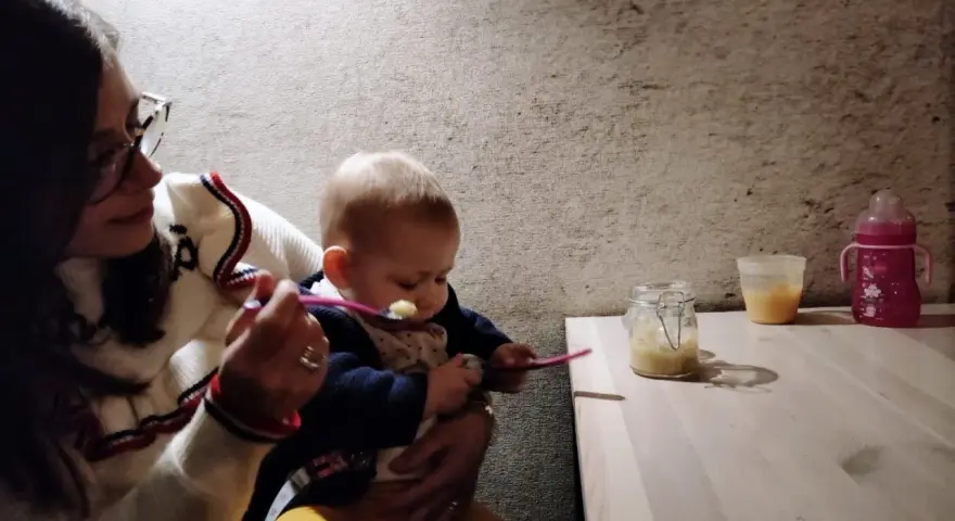 Mamma dà la pappa al suo bimbo fuori casa, con un vasetto di omogeneizzato e un biberon pronti.