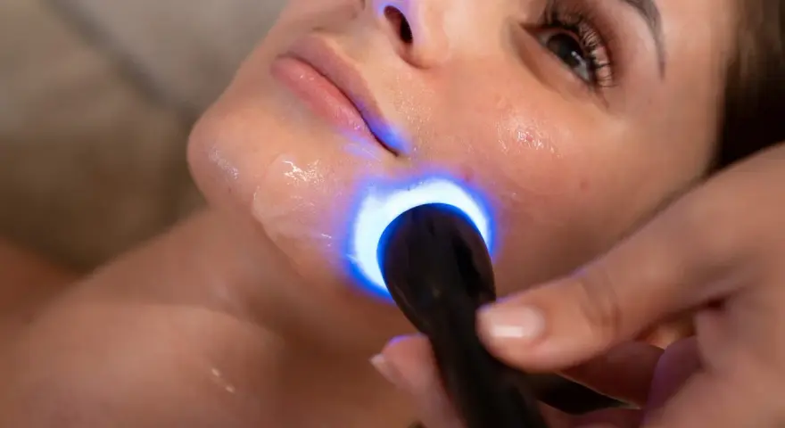 Primo piano del viso di una donna durante un trattamento di biorivitalizzazione con luce blu.