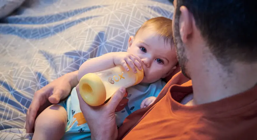 Un padre tiene un biberón per dare da mangiare al suo neonato. Il bambino afferra il biberon con le sue manine.
