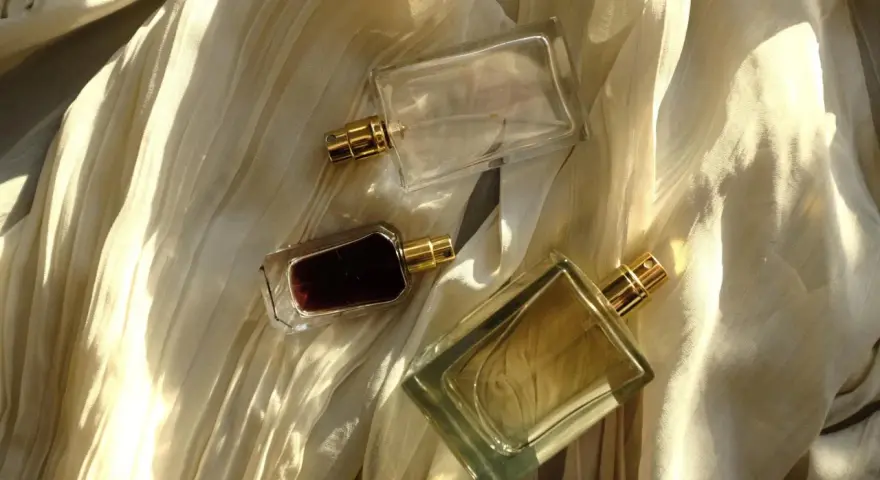Flaconi di profumo su tessuto drappeggiato. Scopri come far durare di più il profumo con questi consigli.