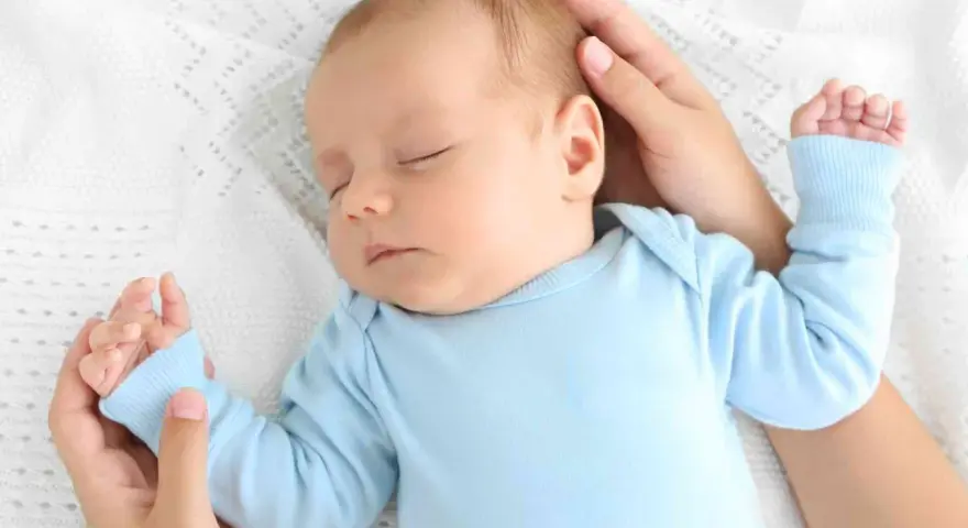 Un adorabile neonato dorme sereno sul fianco, cullato da mani amorevoli su una coperta bianca.