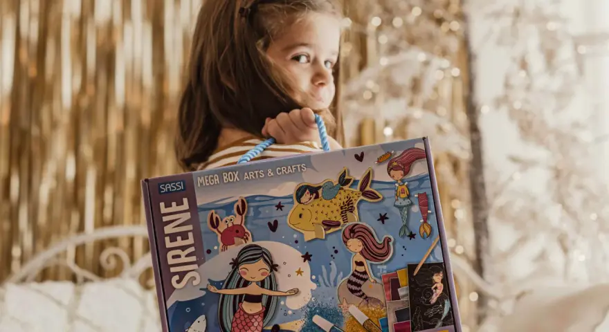 Bambina con scatola "Sirene Mega Box Arts & Crafts". A che età si impara a leggere? Forse con questo kit creativo, l'apprendimento sarà più divertente!