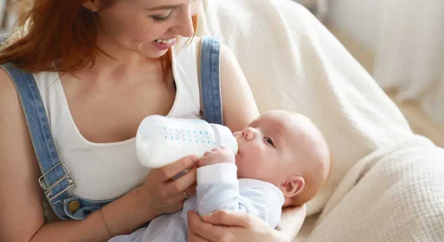 Mamma con capelli rossi allatta il suo bambino con un biberon. Impara come lavare i biberon per garantire l'igiene.