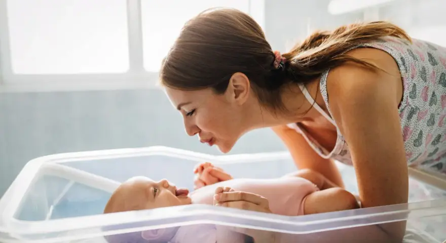 Mamma sorride al suo neonato nella culla. Un momento dolce che fa pensare a cosa mangiare dopo il parto per recuperare le energie.