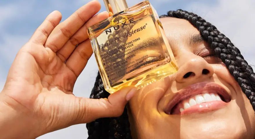 Una mano tiene una bottiglietta di Nuxe Huile Prodigieuse, un olio multiuso per viso, corpo e capelli. Scopri a cosa serve questo prezioso olio.