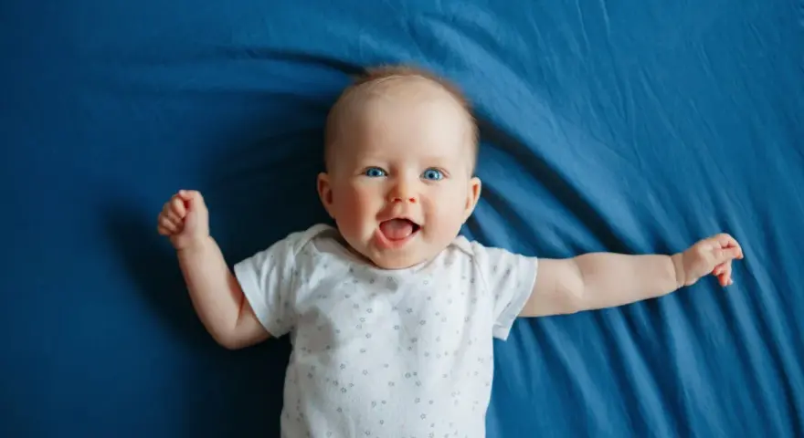 Un bimbo sorridente, con occhi azzurri e braccia aperte, celebra il suo scatto di crescita di 4 mesi su un telo blu.